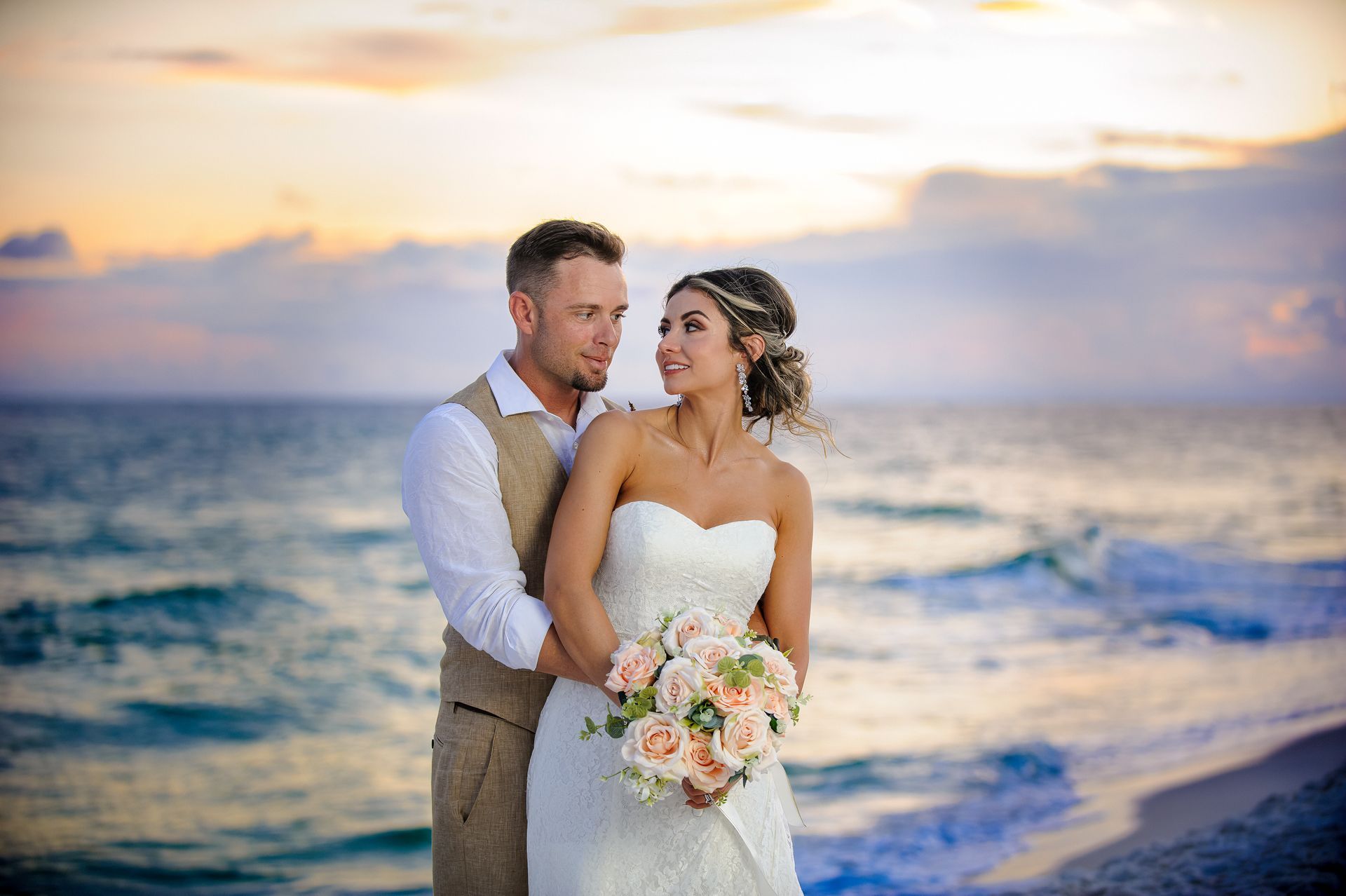 bride and groom embracing on beach at sunset