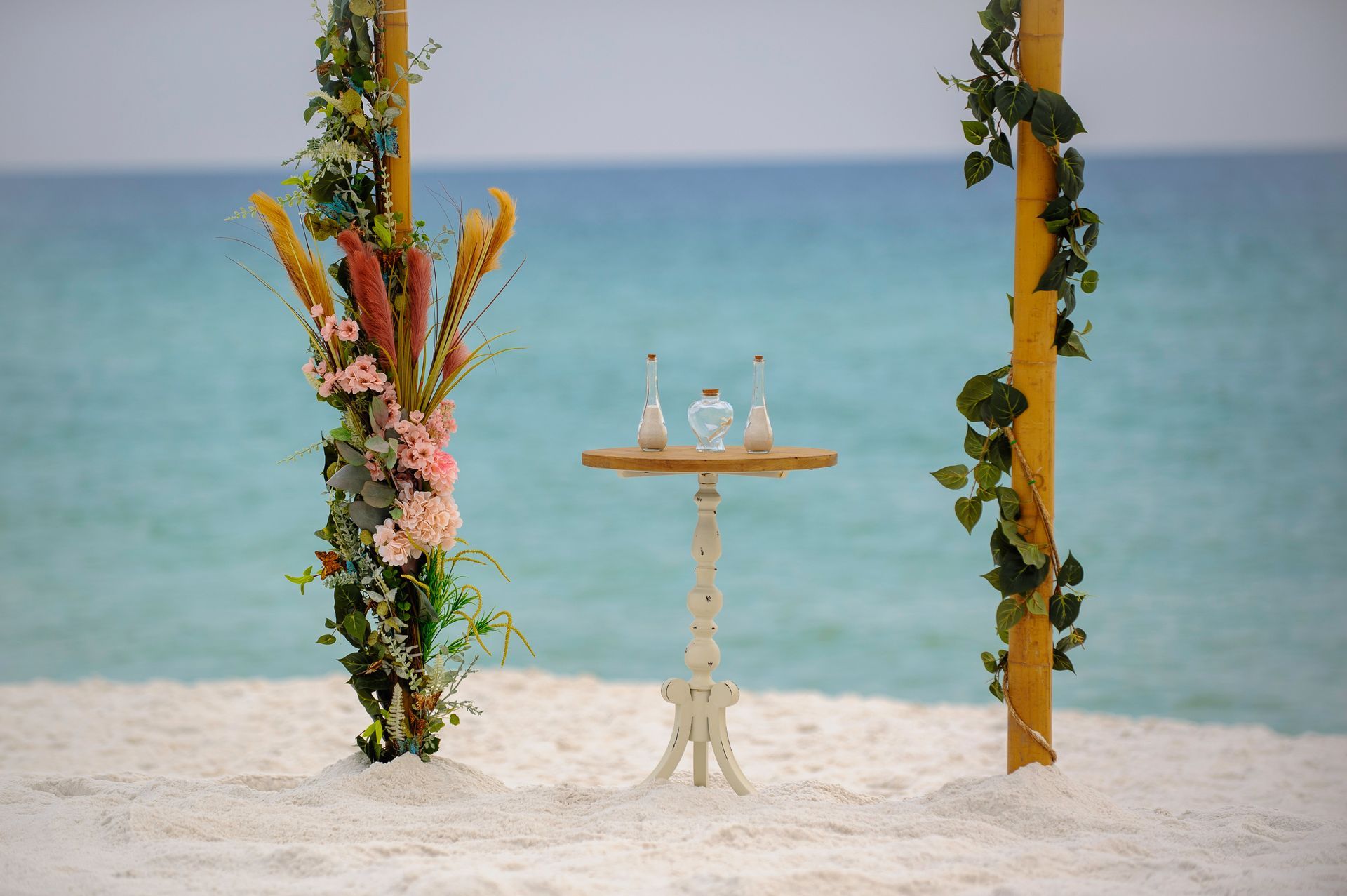 Beach wedding setup with floral arches and a small table by the sea