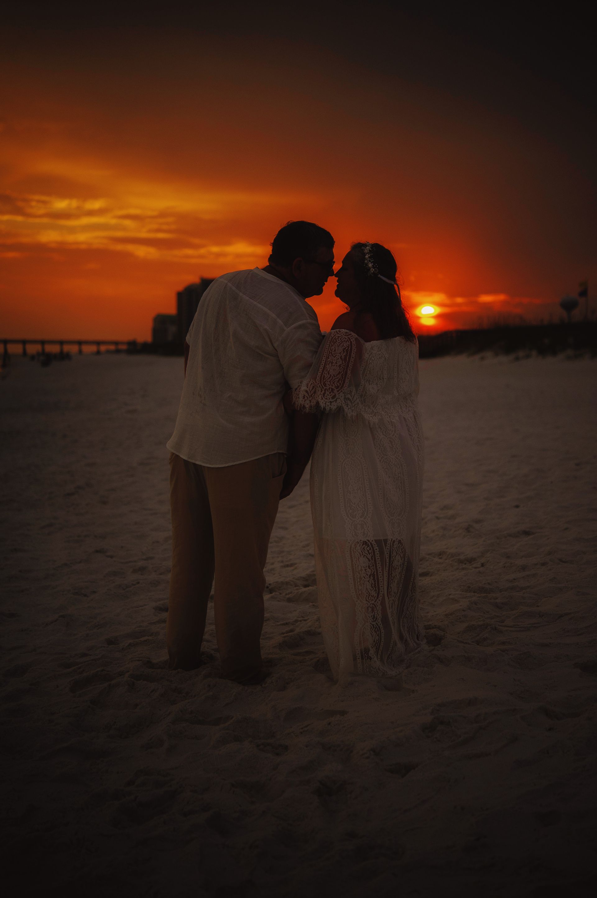 Two people standing on a beach at sunset, silhouetted against an orange sky.