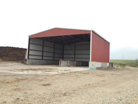 Red metal barn in a rural area, open-sided, concrete foundation, overcast sky.