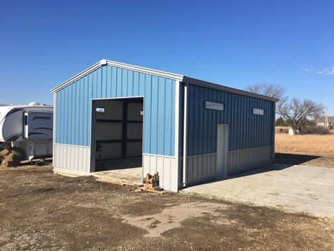 Blue and gray metal building with an open garage door, in an outdoor setting.