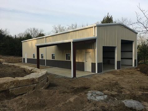 Tan and gray metal building with a covered porch and garage doors; outdoors.