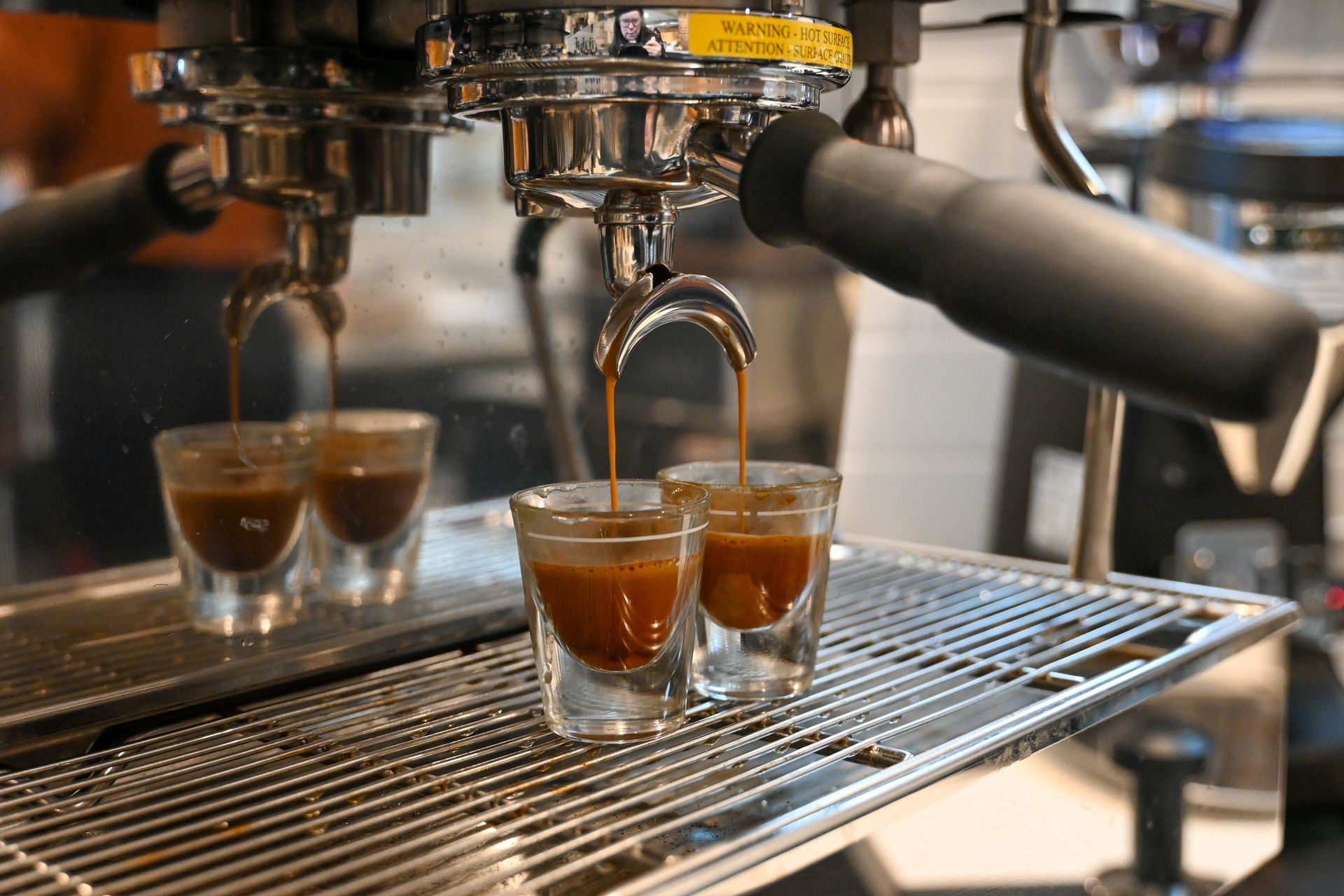 Two shot glasses of espresso are being poured from a coffee machine.