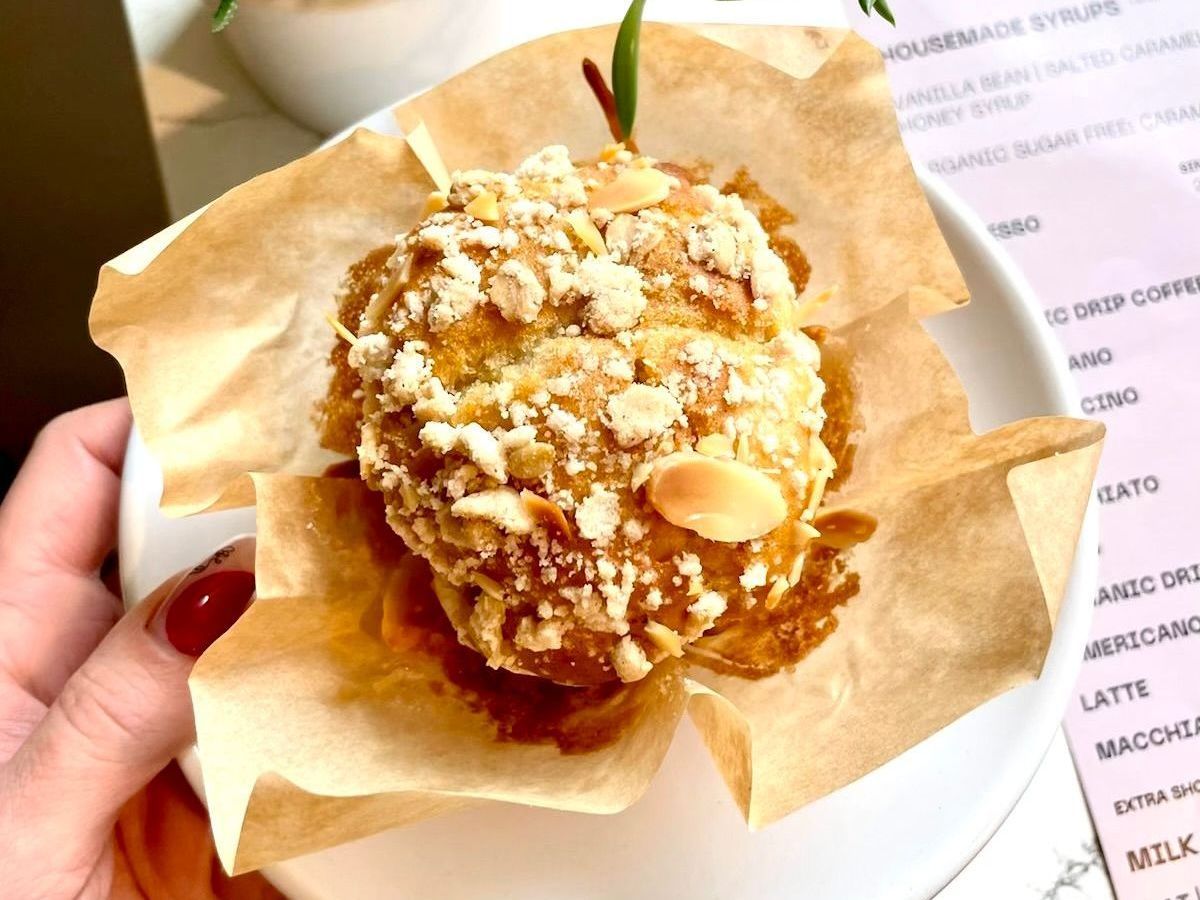 A person is holding a muffin with nuts on top of it.