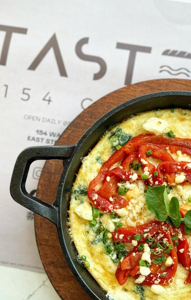 An omelet with tomatoes and cheese is sitting on a wooden cutting board in front of a sign that says taste 154