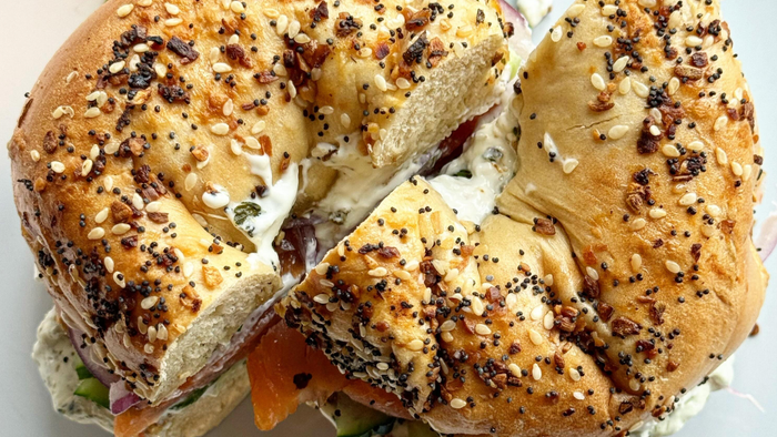 A bagel sandwich with a slice taken out of it on a plate.