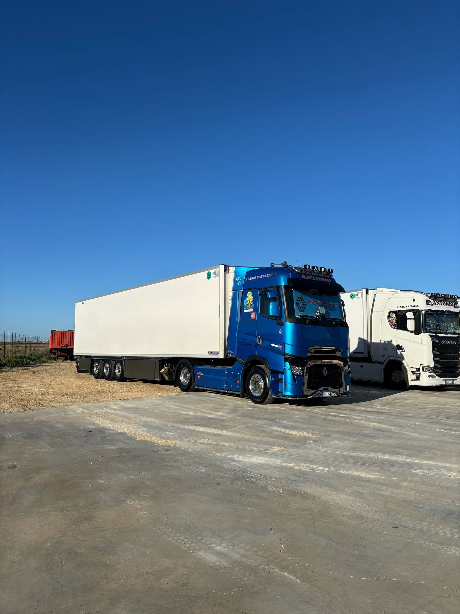 Un camion blu è parcheggiato accanto a un camion bianco in un parcheggio.