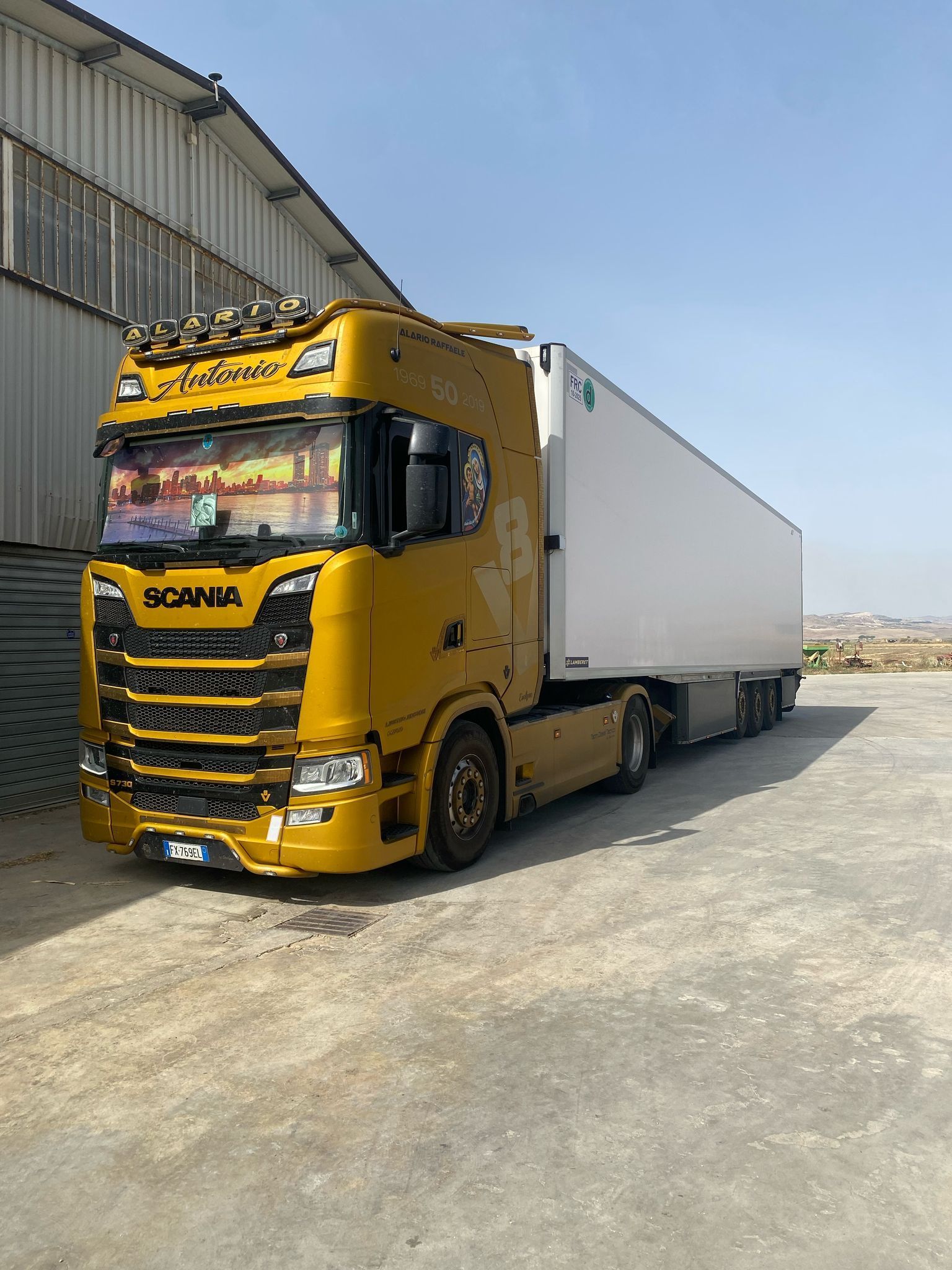 Un camion giallo con un rimorchio bianco è parcheggiato davanti a un edificio.