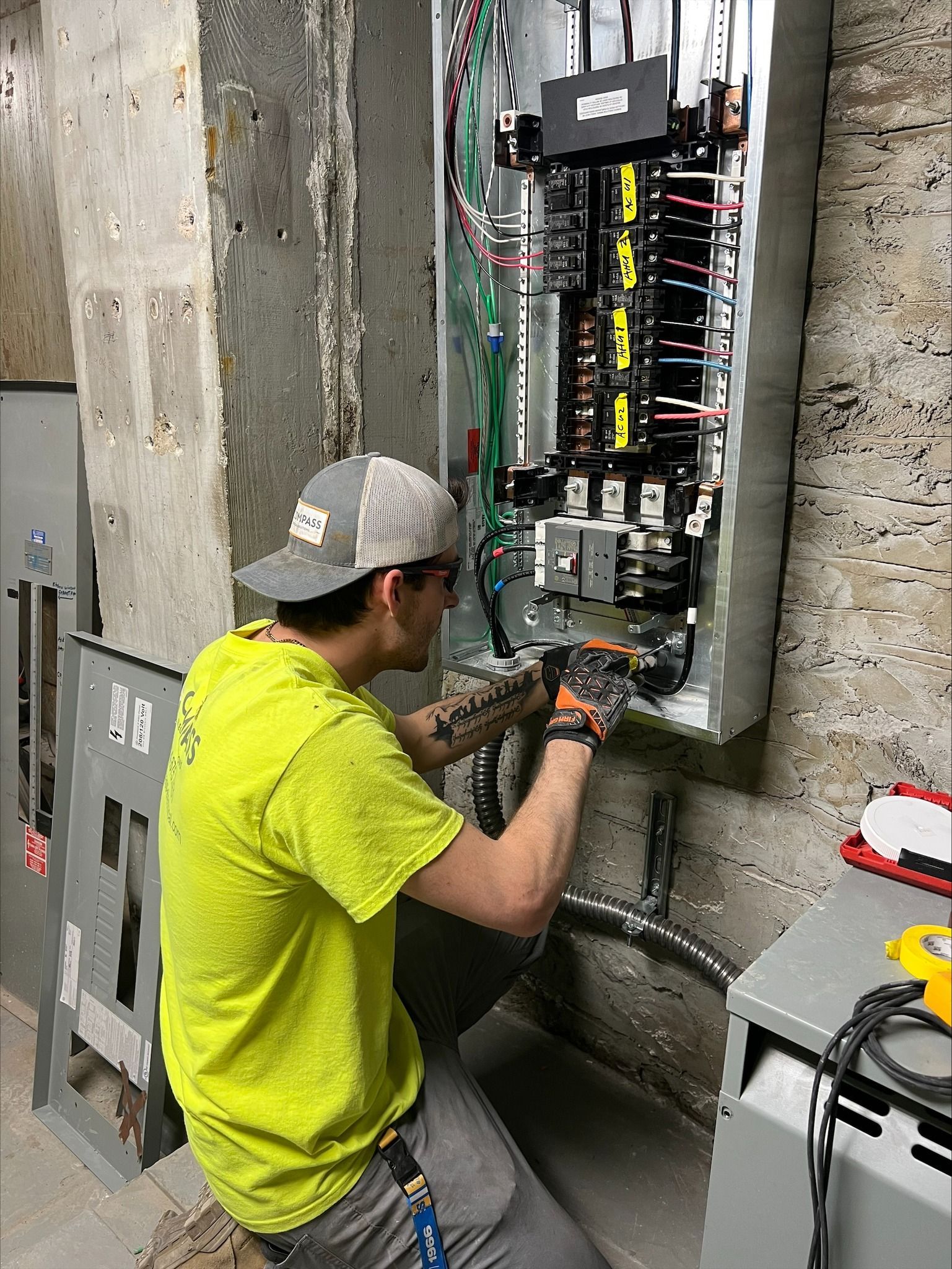 Electrician working on an open circuit breaker panel in a concrete utility room.