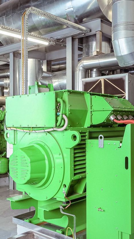 Bright green industrial machine in a factory with metal ducts and pipes overhead
