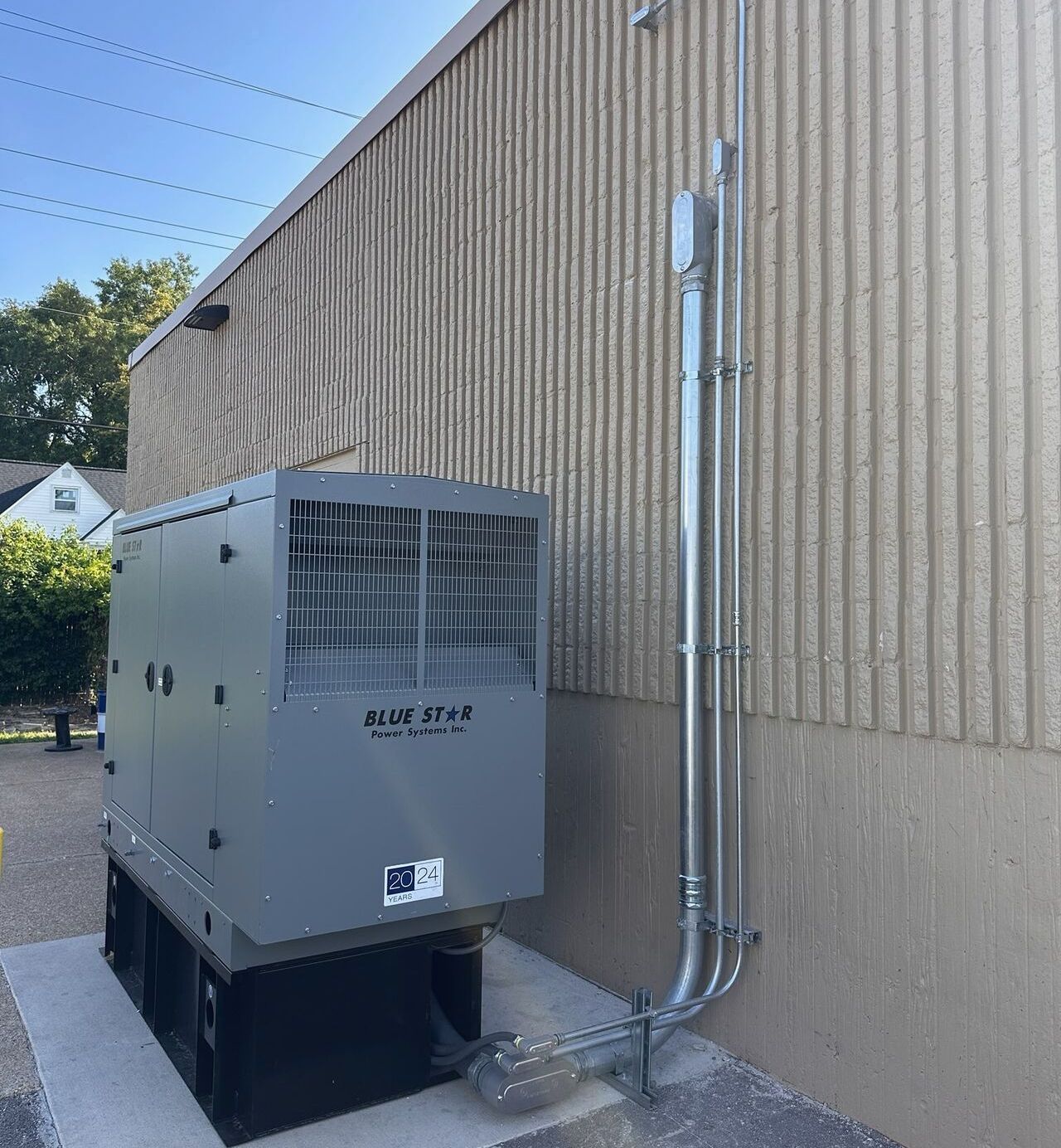 Gray generator next to a tan building with conduit pipes running up the wall.