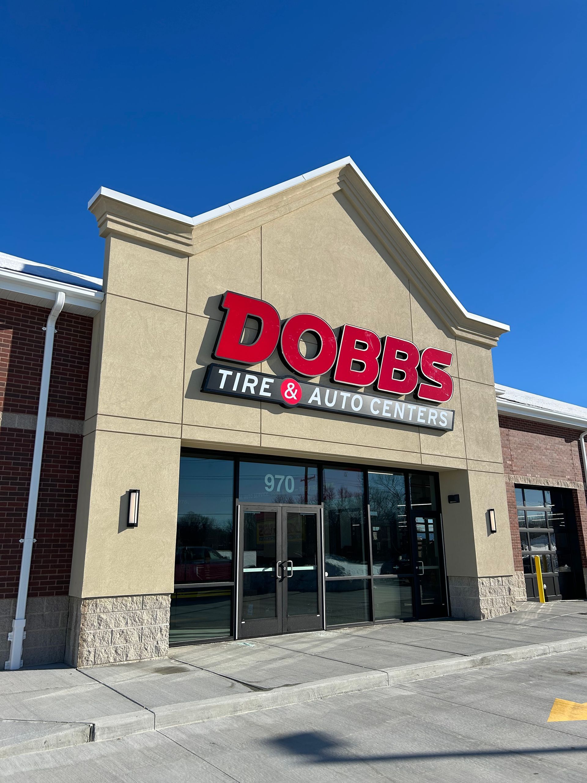 Dobbs Tire & Auto Center store front, tan building with red signage, blue sky.