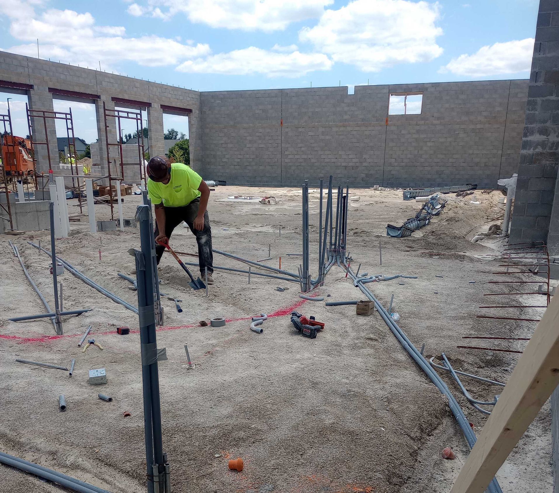 Construction worker bending over rebar at a building site with unfinished cinderblock walls and gravel ground