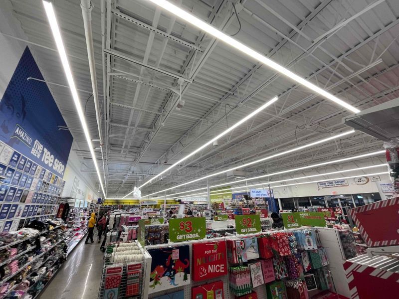 Bright retail store aisle with white ceiling lights and colorful holiday merchandise displays.