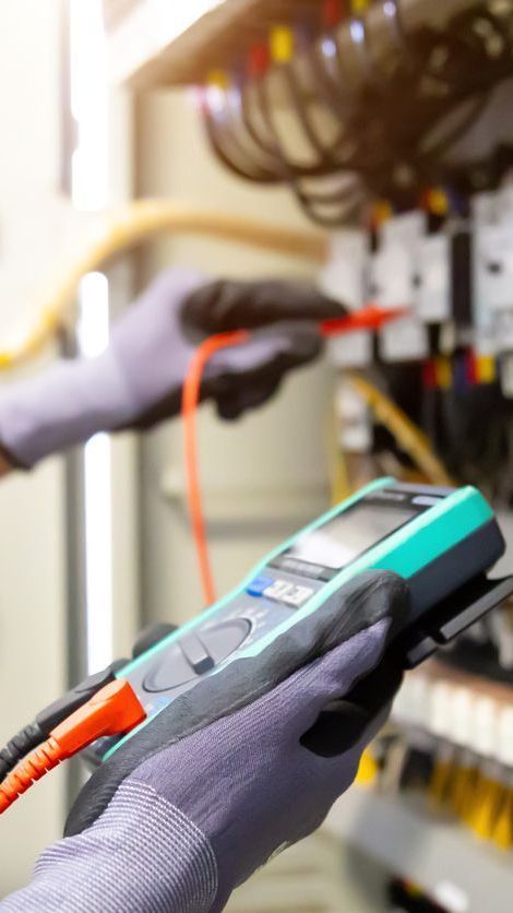 Gloved hands testing an electrical panel with a handheld multimeter and red probe.