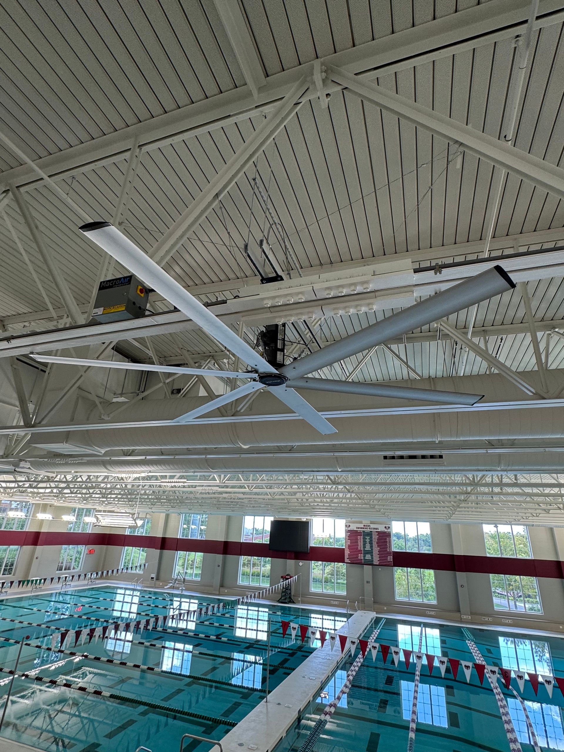 Indoor swimming pool with lanes, high ceiling fans, and bright windows along the far wall