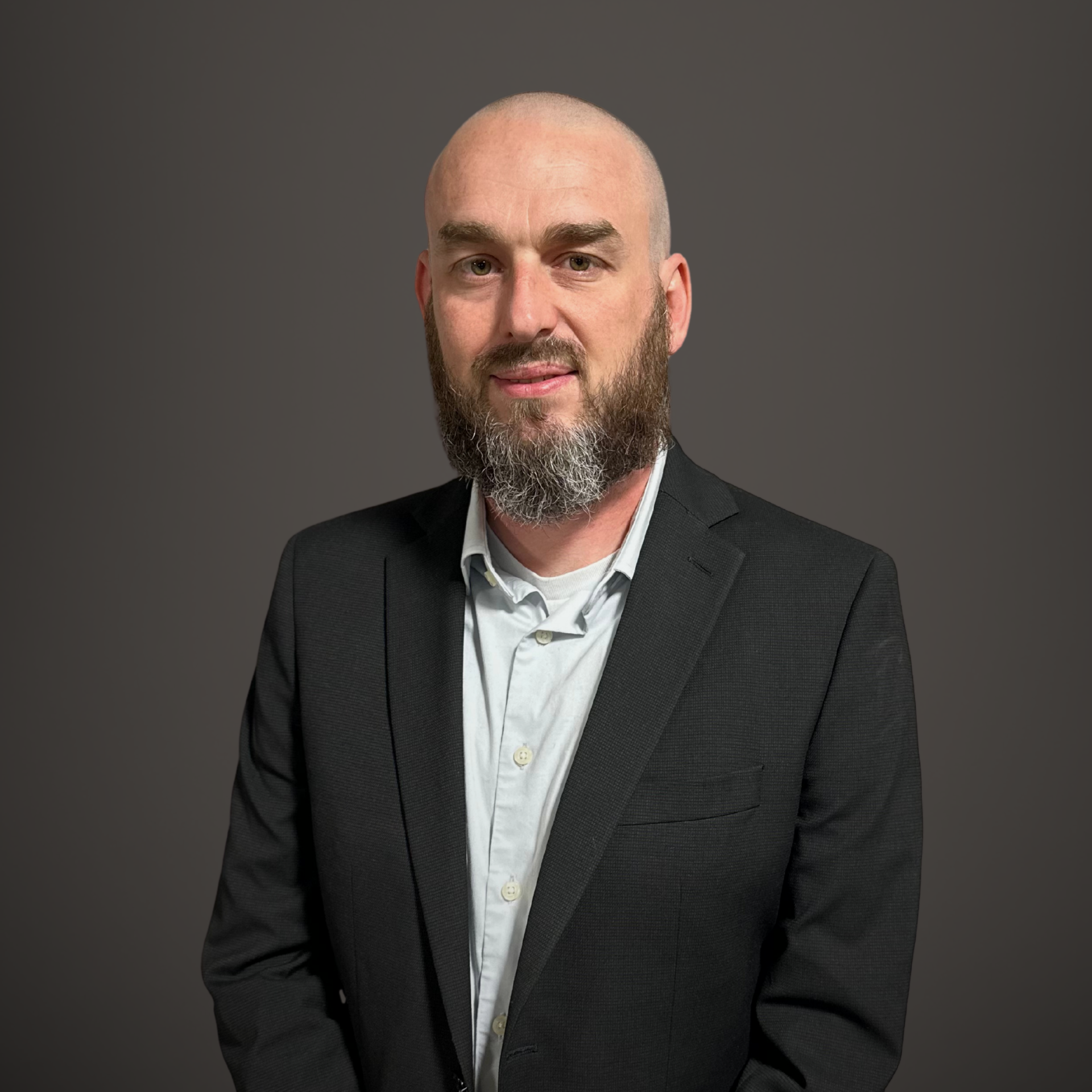 Portrait of a bald man with a beard in a dark suit against a plain gray background