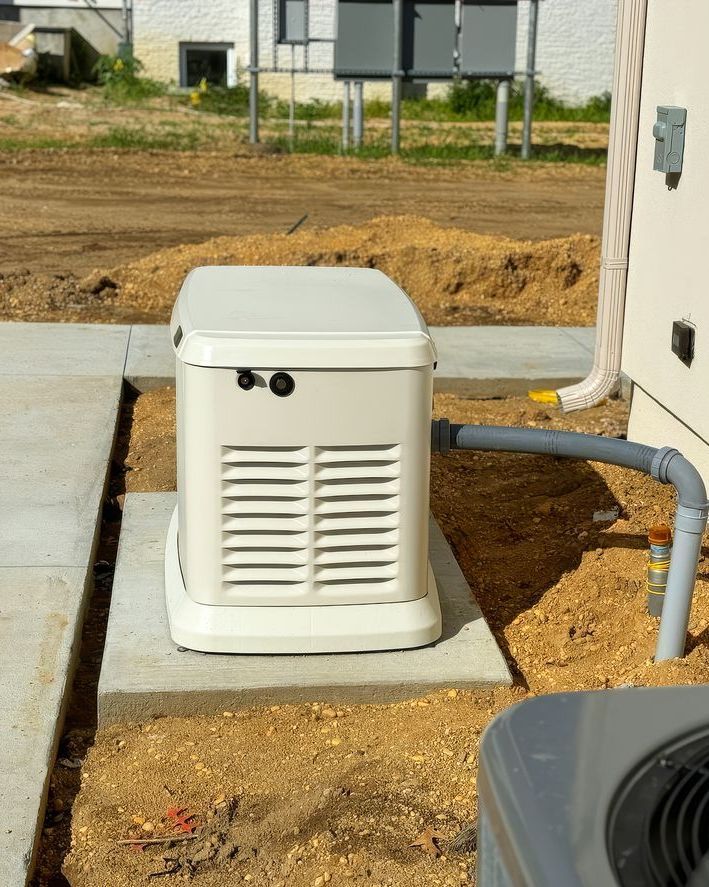 White outdoor generator on a concrete pad beside a house, with gray conduit pipe and bare dirt yard.