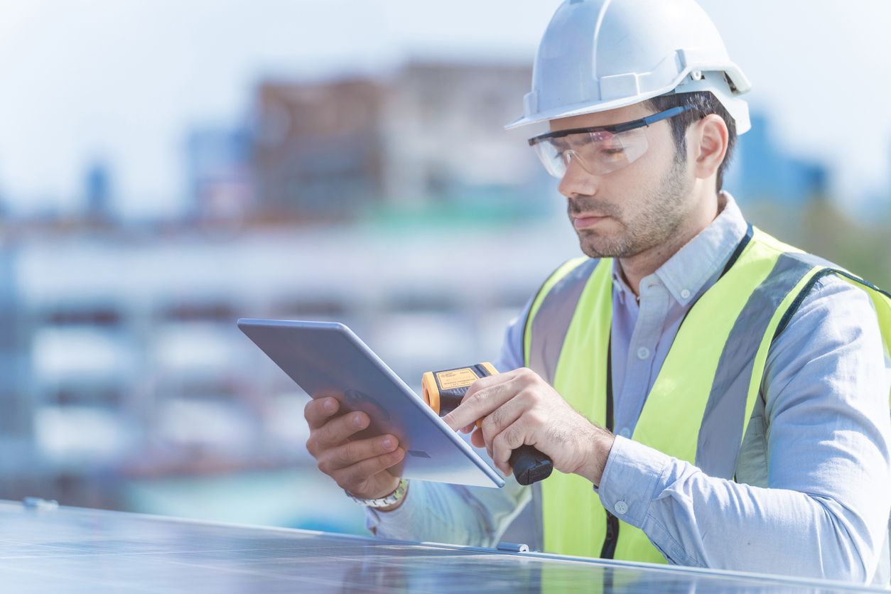 Construction worker in white hard hat and safety vest using a tablet at a building site