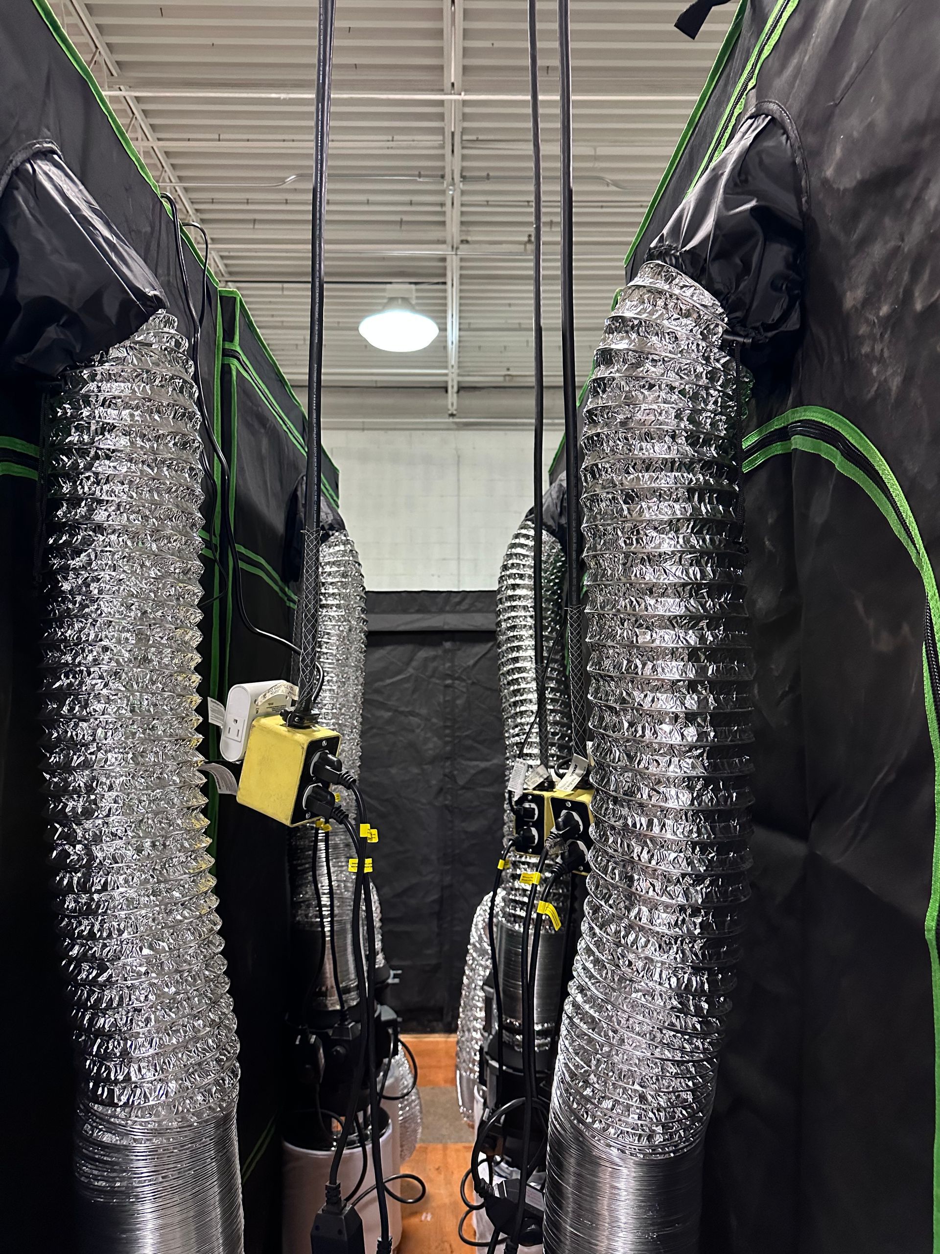 Narrow indoor aisle with black server racks and silver insulated ducts in a data center-like room