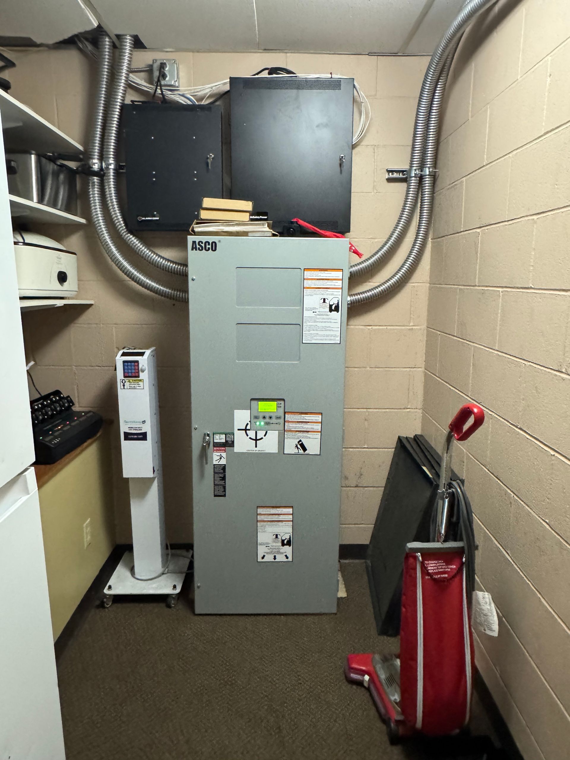 Mechanical room with gray HVAC/furnace unit, exposed ductwork, and a red vacuum cleaner along the wall.