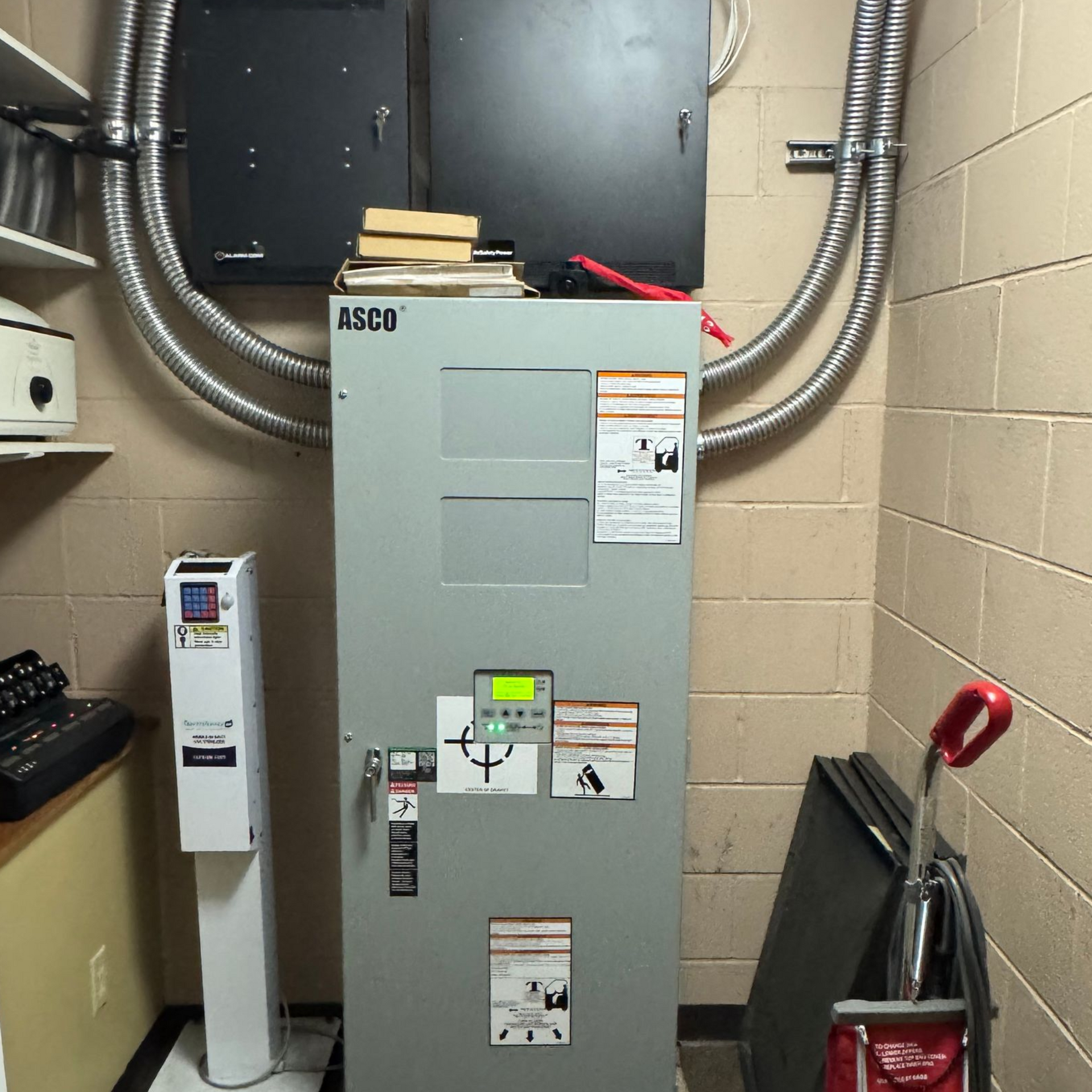 Utility room with a gray electrical panel, silver ducts, and cleaning supplies against beige cinderblock walls.