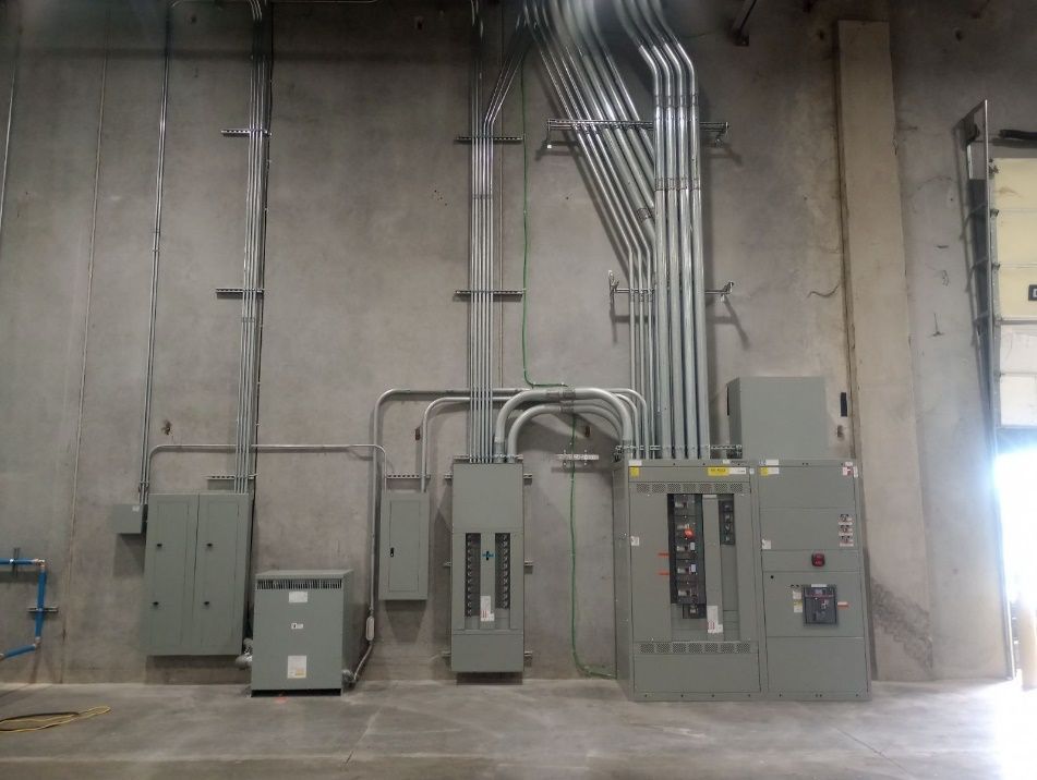 Electrical panel and conduit installation on a concrete wall in an industrial setting.