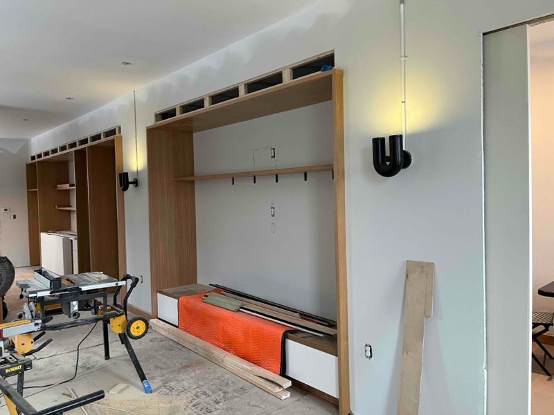 Interior under construction with built-in wooden shelving, orange bench, and black wall sconces.