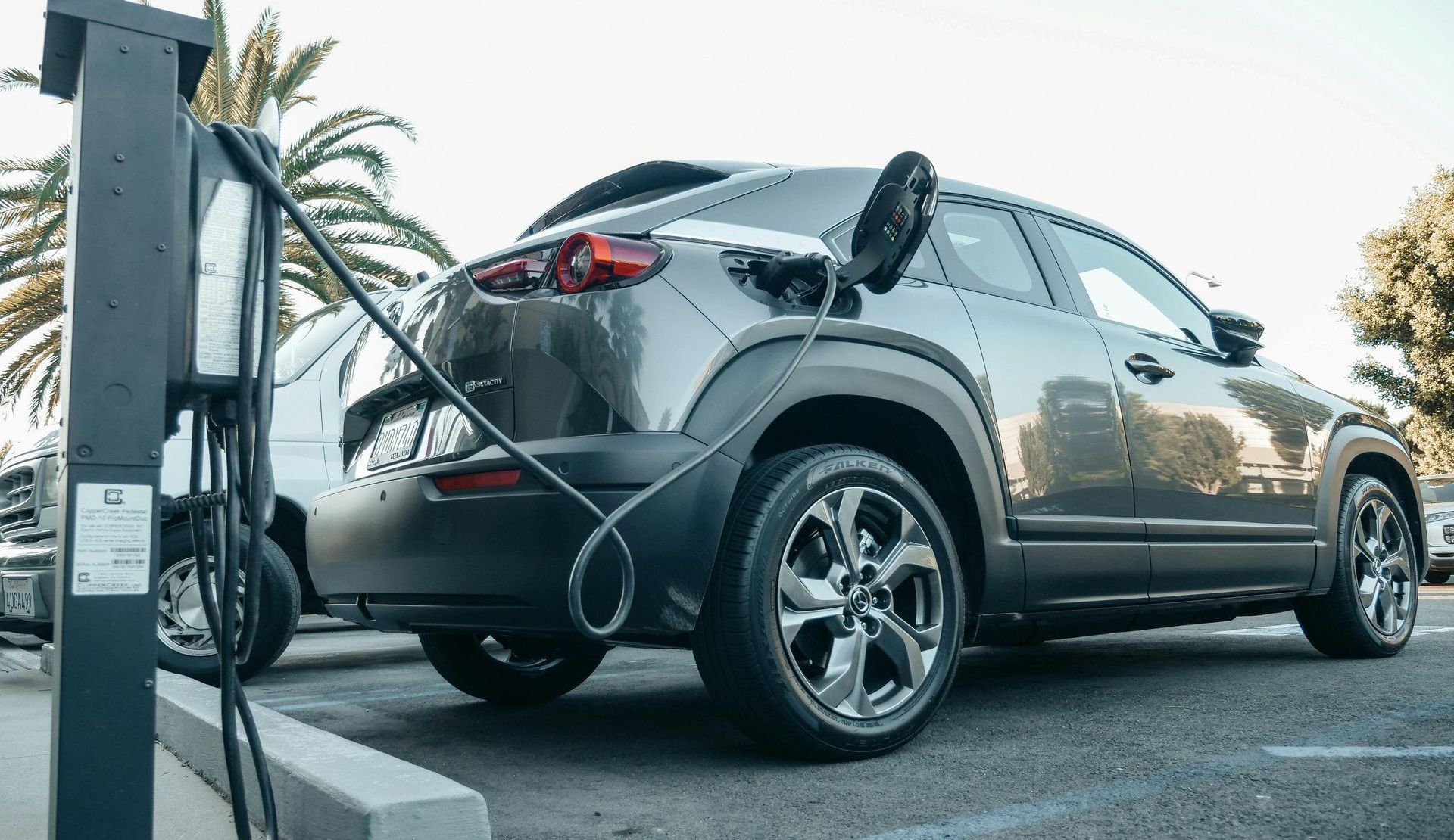 Gray electric car charging at a station outdoors.