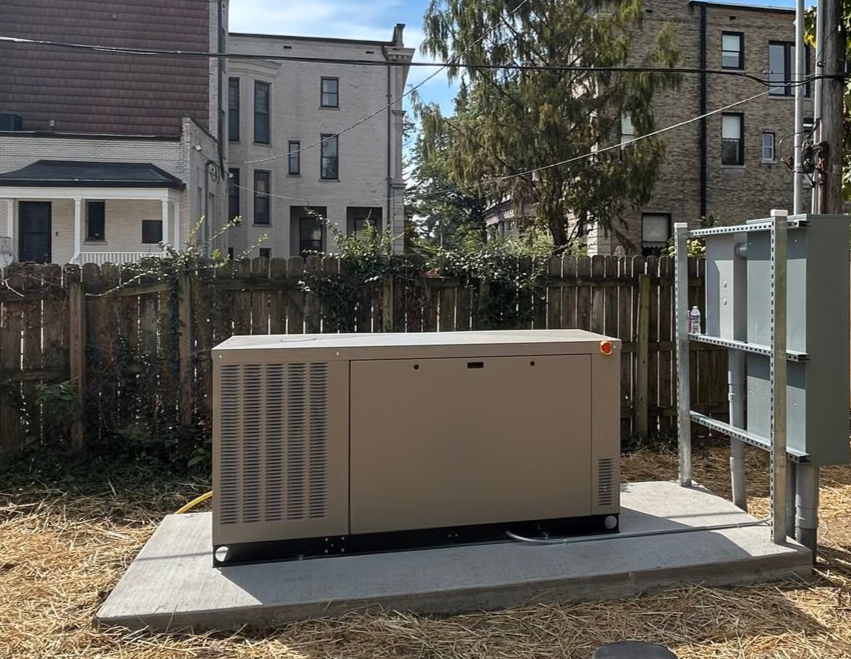 Beige outdoor generator on a concrete pad beside a fence in a backyard
