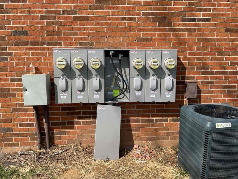Electrical meters and utility boxes mounted on a brick wall beside outdoor HVAC equipment.