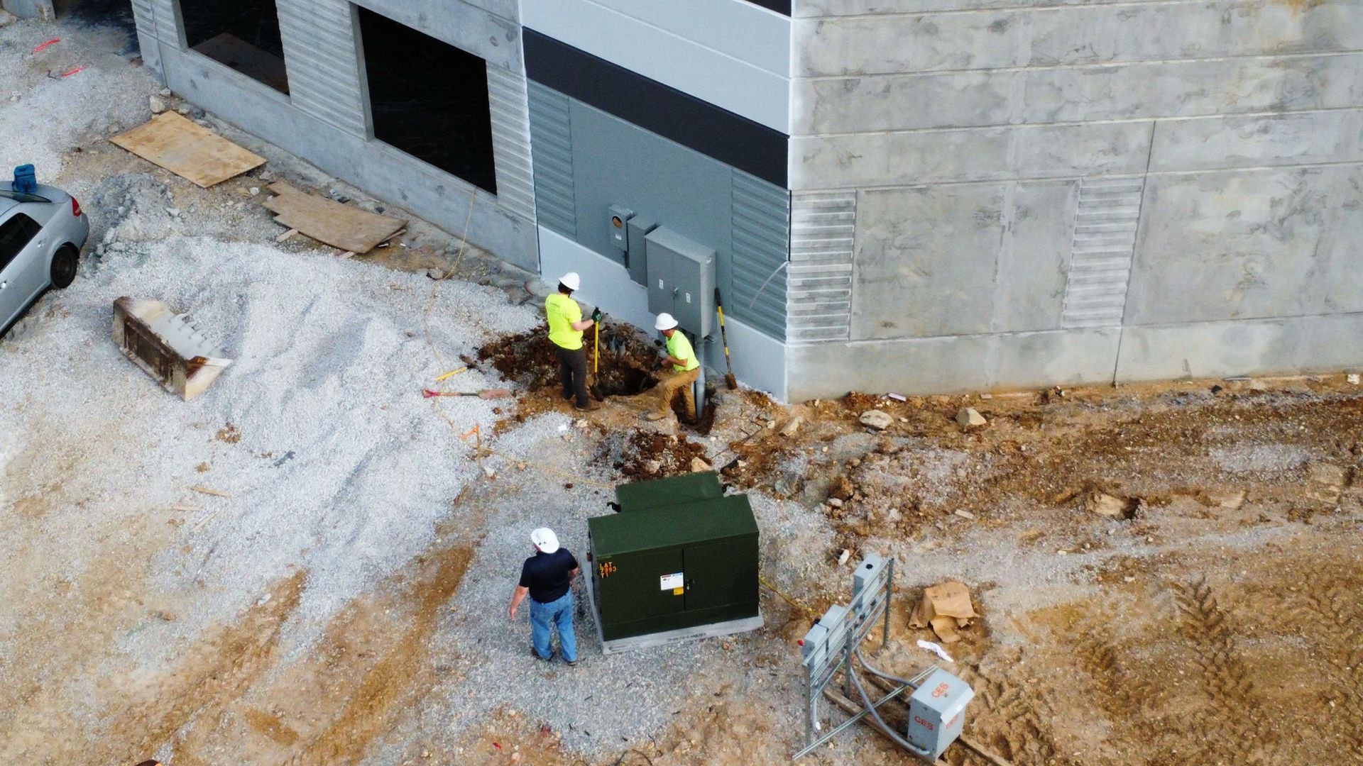 Construction workers installing electrical equipment near a building.