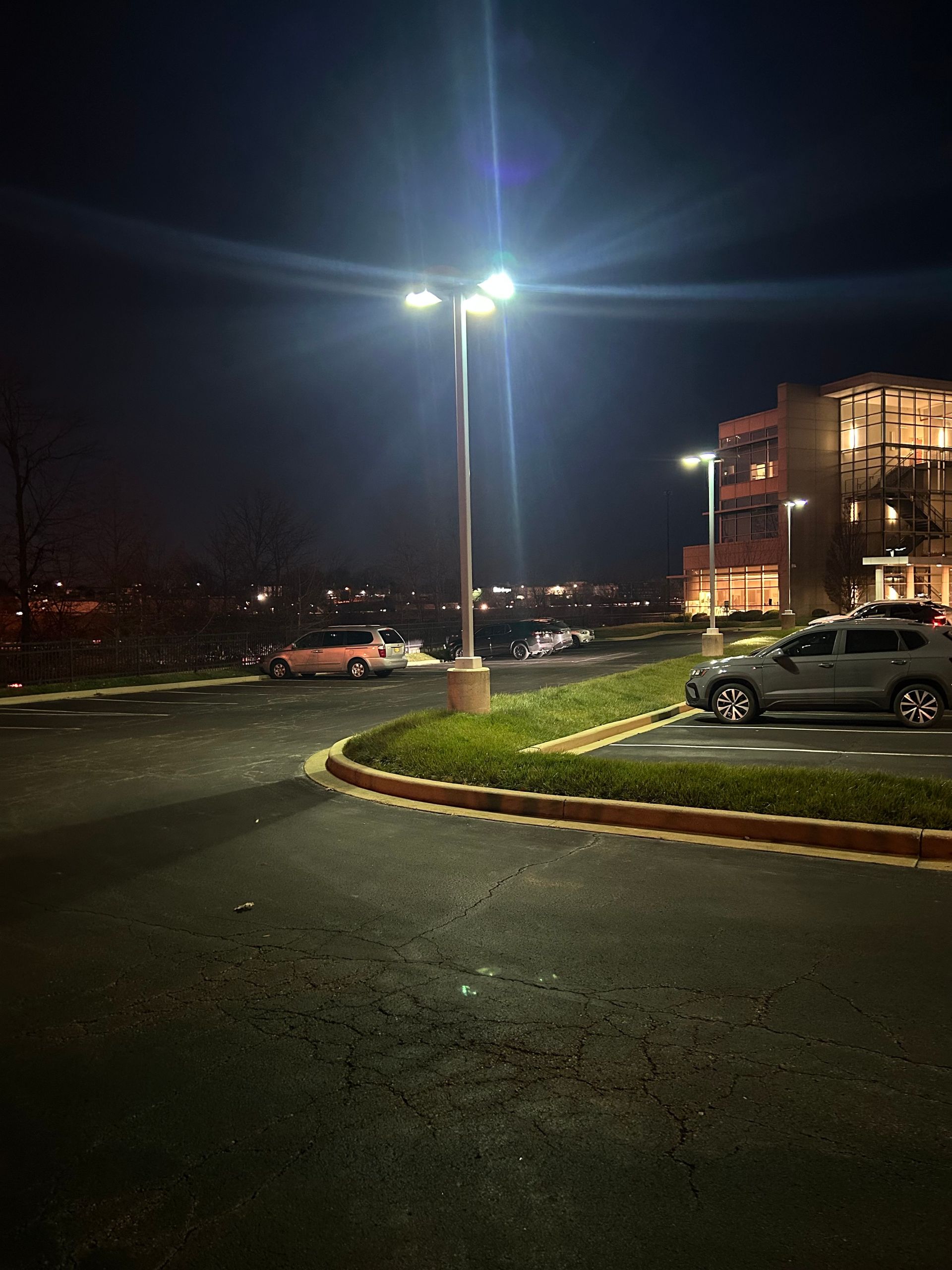 Night parking lot with bright streetlights, parked cars, and a lit building in the background.
