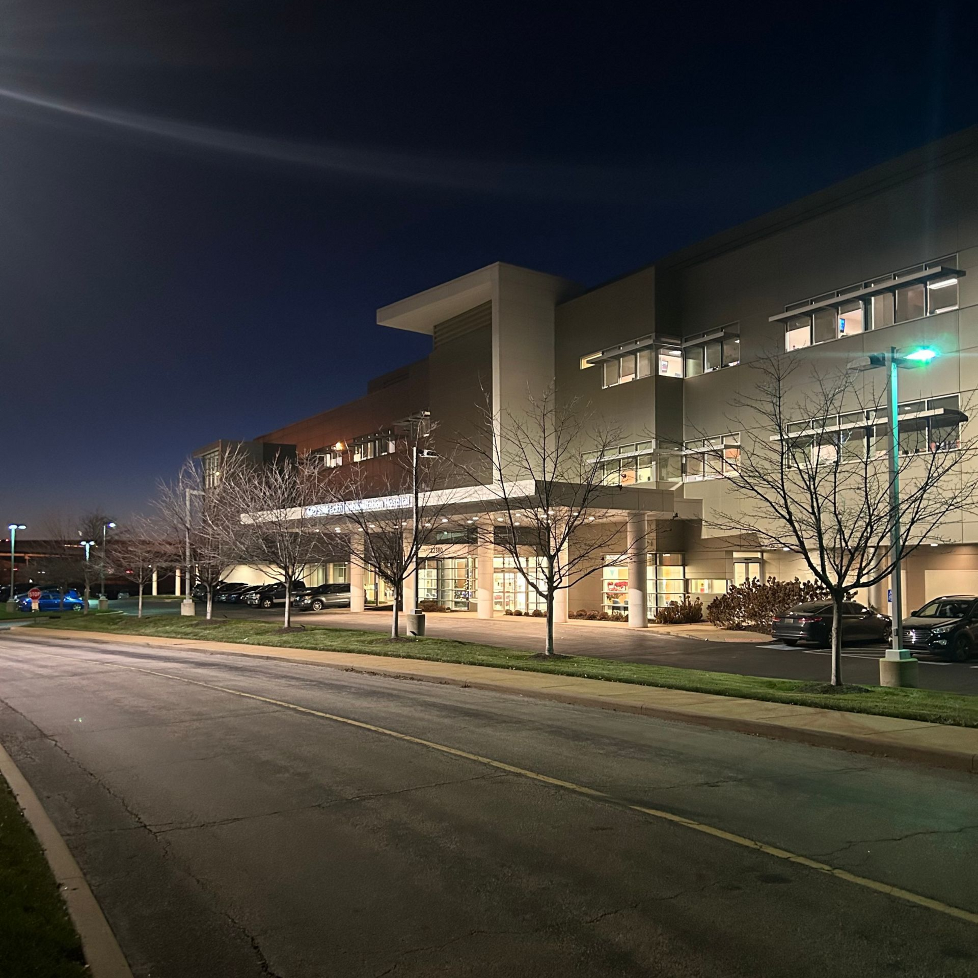 Hospital building at night with lighted entrance and streetlights.
