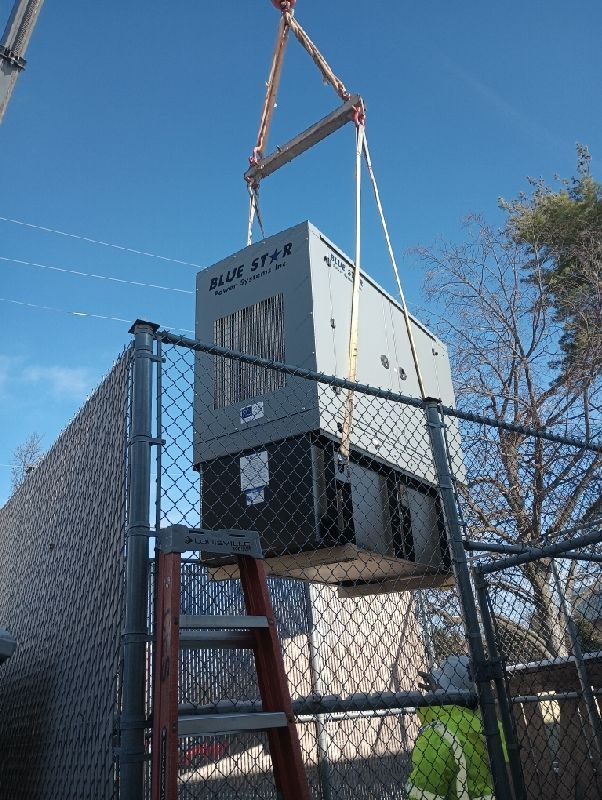 A Blue Star unit is lifted by a crane over a chain-link fence on a sunny day.