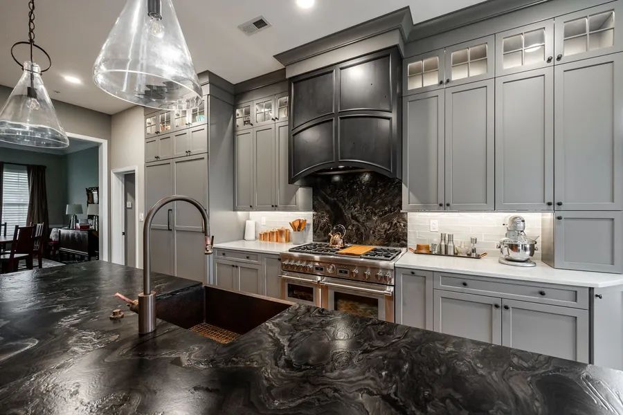 A kitchen with gray cabinets , black counter tops, a sink, and a stove.