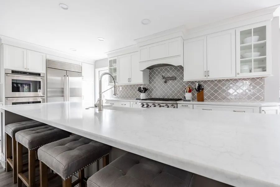 A kitchen with white cabinets, white counter tops, and stools.