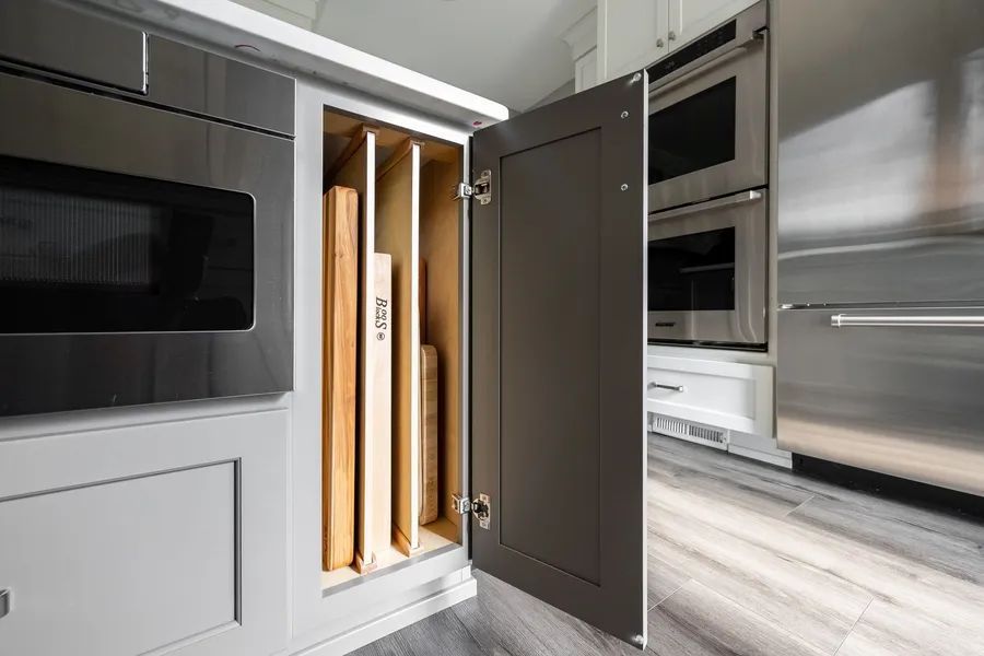 A kitchen with stainless steel appliances and cutting boards in a cabinet.
