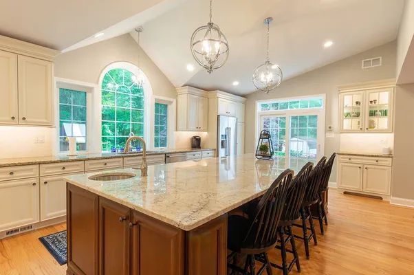 A kitchen with a large island , sink , chairs and a large window.