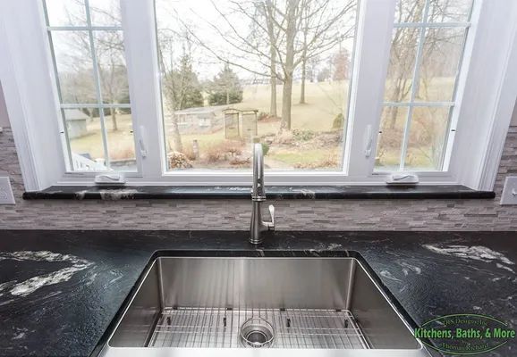 A kitchen sink is sitting under a window with a view of a field.