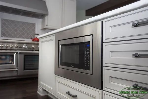 A kitchen with white cabinets and a stainless steel microwave oven.