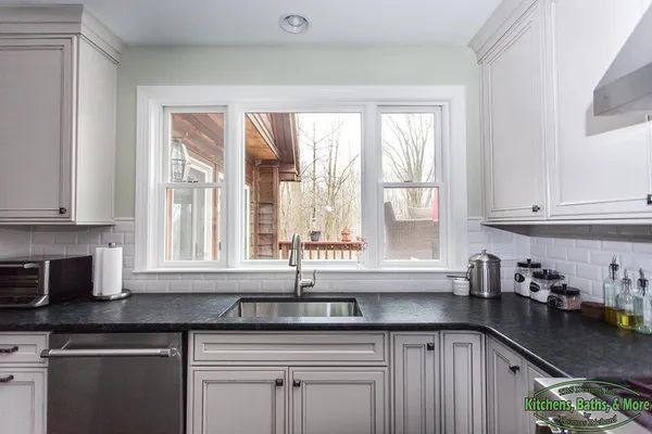 A kitchen with white cabinets, black counter tops, a sink and a window.