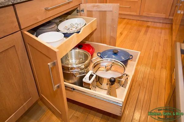 A wooden drawer filled with pots and pans in a kitchen.