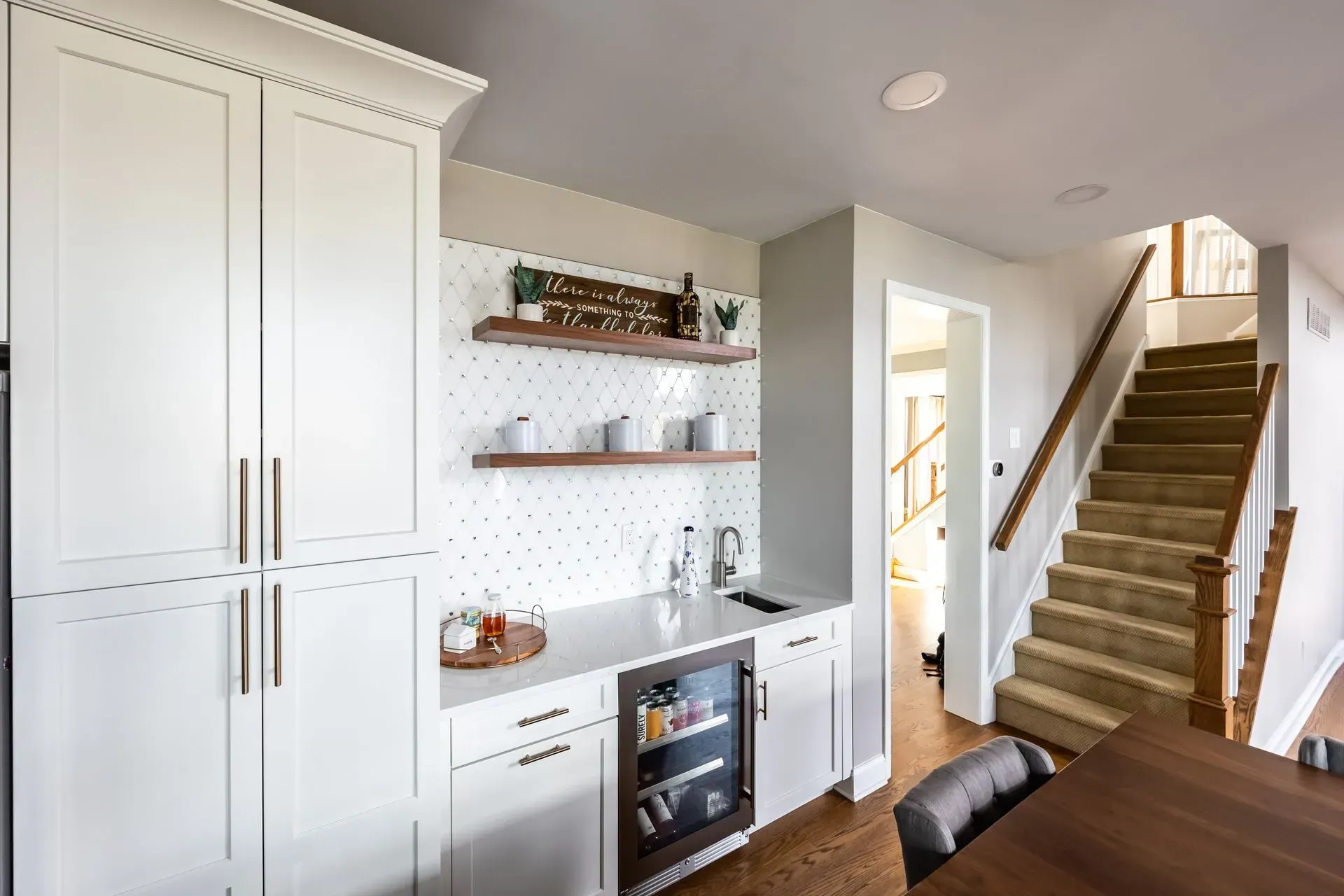 A kitchen with white cabinets, a refrigerator, a sink and stairs.