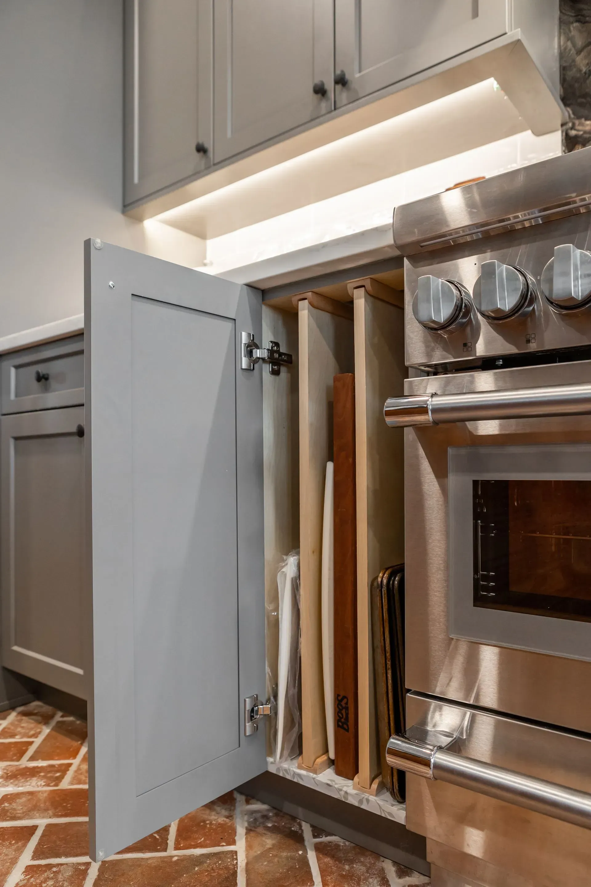 A kitchen with stainless steel appliances and a cutting board holder in the cabinet.