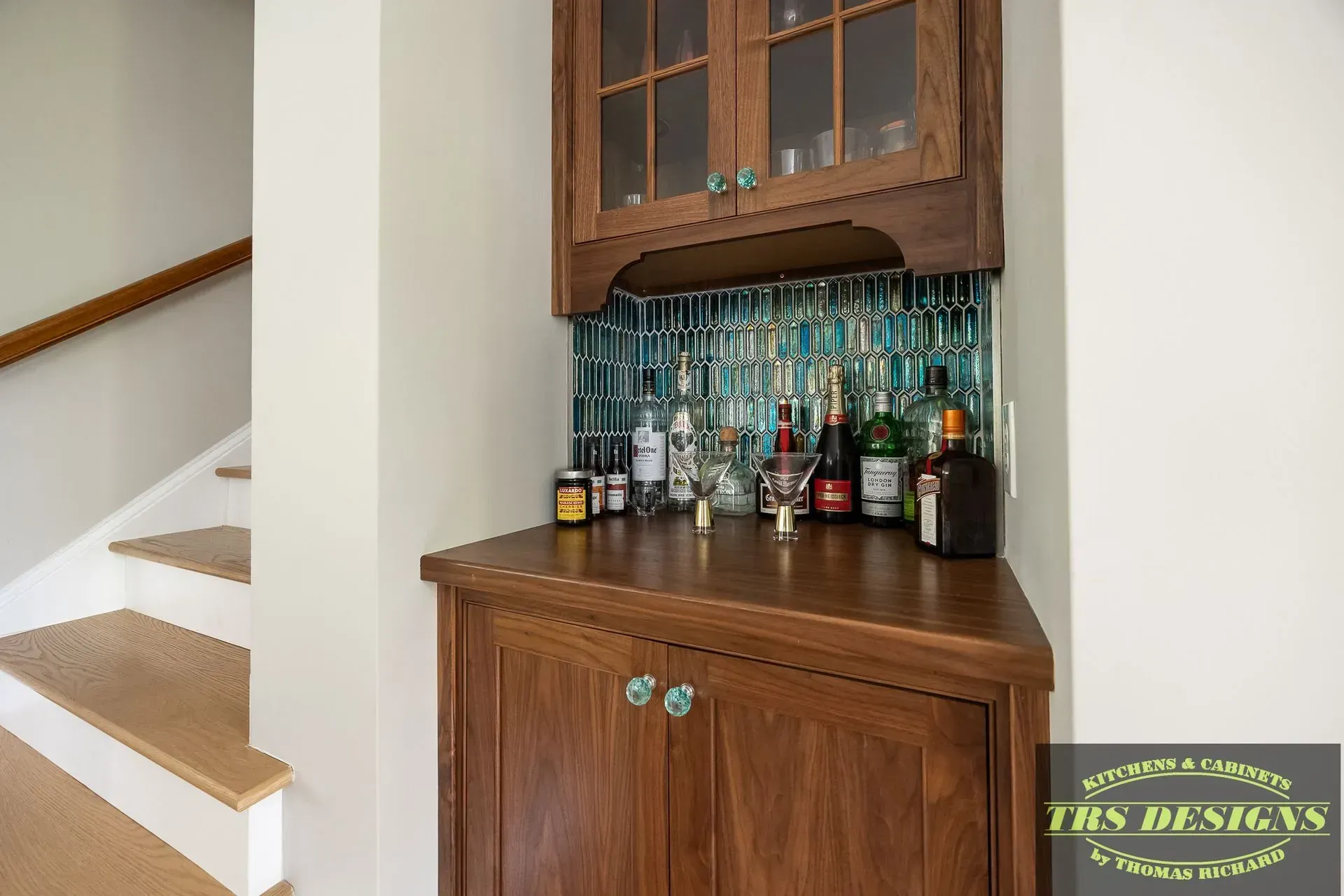 A bar with bottles of liquor on it in a room next to stairs.