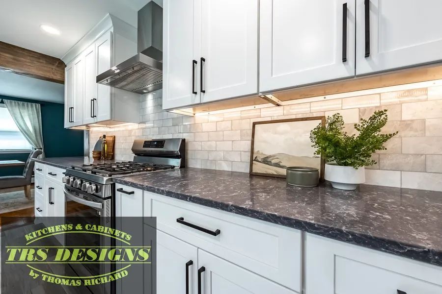 A kitchen with white cabinets and black counter tops.