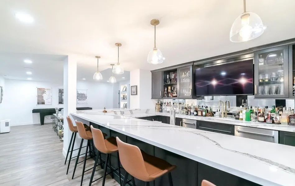 A kitchen with a bar and stools and a lot of bottles on the counter.