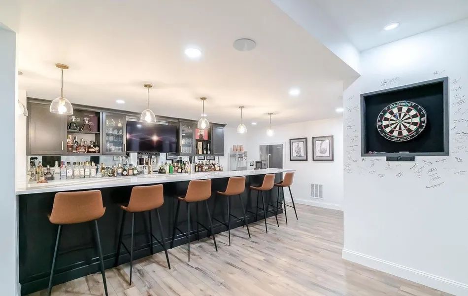 A bar with stools and a dart board on the wall in a basement.