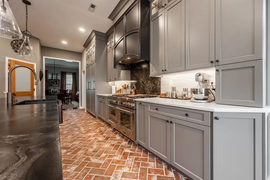 A kitchen with gray cabinets and a brick floor.